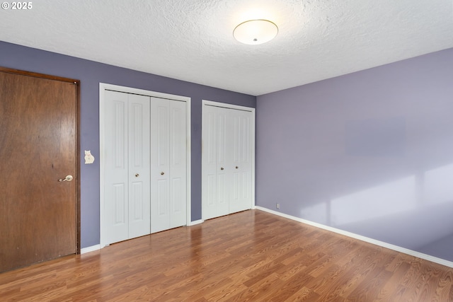 unfurnished bedroom with hardwood / wood-style floors, a textured ceiling, and multiple closets