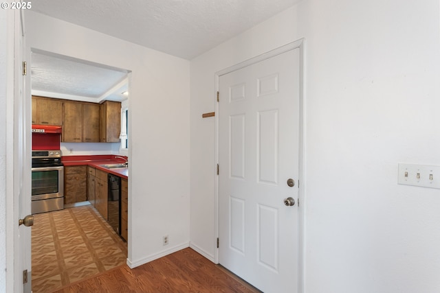 kitchen featuring stainless steel electric range oven, black dishwasher, sink, hardwood / wood-style flooring, and a textured ceiling