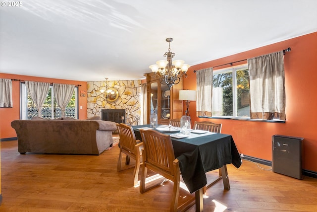 dining space with a notable chandelier, a healthy amount of sunlight, a fireplace, and light wood-style floors