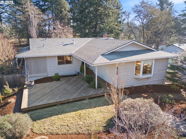 rear view of property featuring a wooden deck, a lawn, and a shingled roof