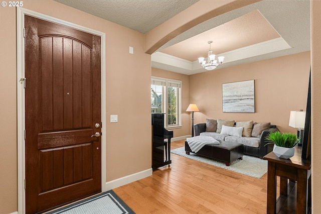 foyer with an inviting chandelier, a tray ceiling, wood-type flooring, and a textured ceiling