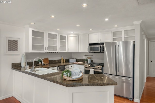 kitchen with a sink, a peninsula, stainless steel appliances, white cabinetry, and open shelves