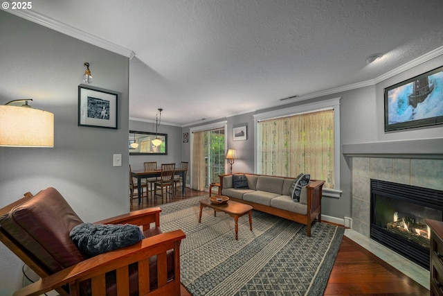 living area featuring ornamental molding, wood finished floors, baseboards, a tiled fireplace, and a textured ceiling