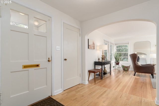 foyer featuring light wood-type flooring, arched walkways, and baseboards