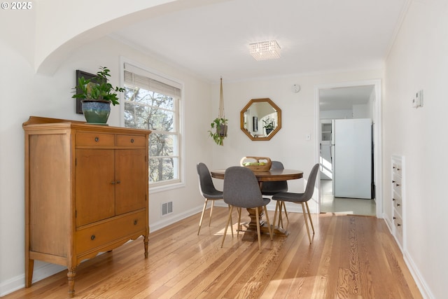 dining room featuring light wood-style flooring, visible vents, and crown molding