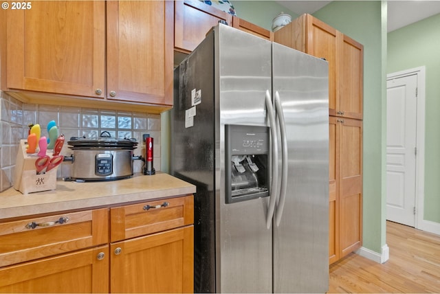 kitchen featuring stainless steel refrigerator with ice dispenser, light wood-type flooring, and decorative backsplash