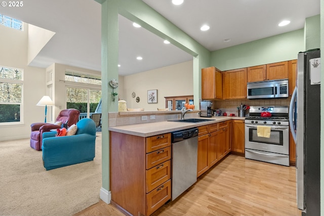 kitchen with sink, stainless steel appliances, light hardwood / wood-style floors, decorative backsplash, and kitchen peninsula