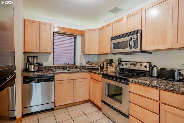 606 NW Naito Pkwy Unit A14, Portland, OR 97209 - kitchen with stainless steel appliances, light brown cabinetry, a sink, dark stone counters, and light tile patterned floors