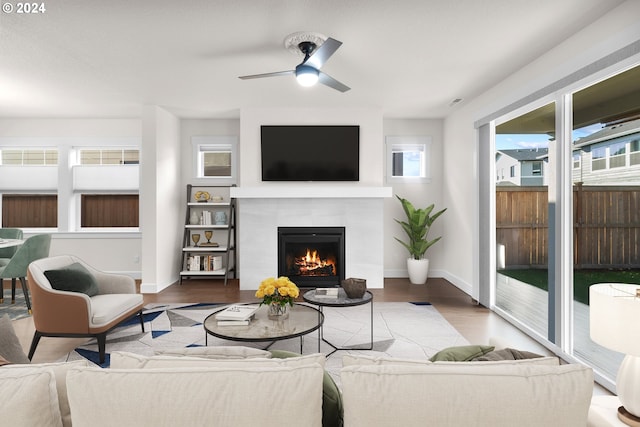 living room with a tiled fireplace, ceiling fan, and wood-type flooring