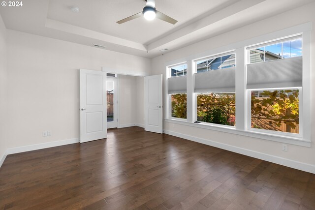 empty room with ceiling fan, a tray ceiling, and dark wood-type flooring