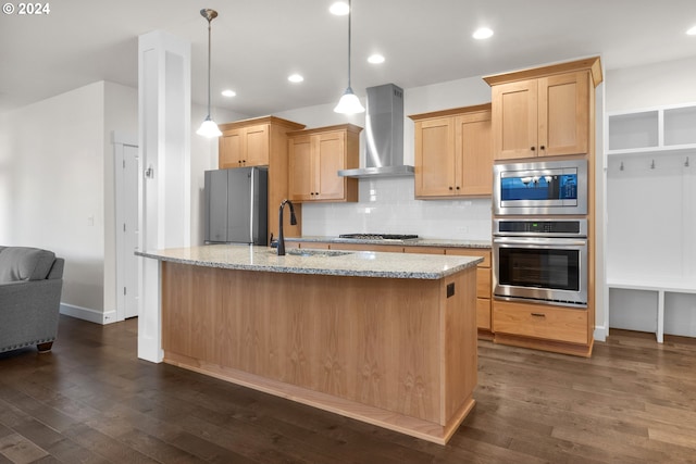 kitchen with stainless steel appliances, hanging light fixtures, light stone counters, sink, and wall chimney range hood