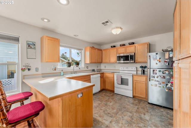 kitchen with visible vents, appliances with stainless steel finishes, a peninsula, light brown cabinets, and a sink