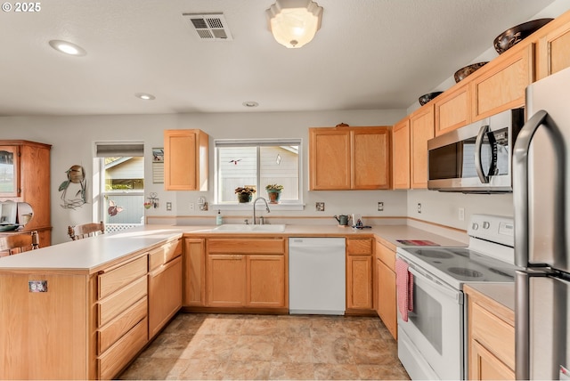 kitchen featuring visible vents, a peninsula, stainless steel appliances, light countertops, and a sink