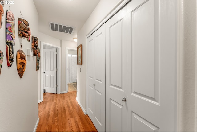 hallway featuring light wood finished floors, baseboards, and visible vents