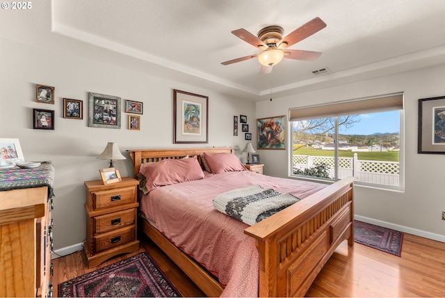 bedroom featuring a raised ceiling, visible vents, a ceiling fan, wood finished floors, and baseboards