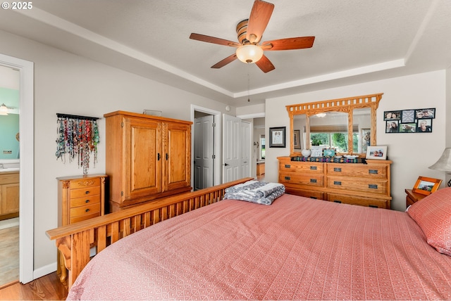 bedroom with ceiling fan, connected bathroom, a raised ceiling, and wood finished floors