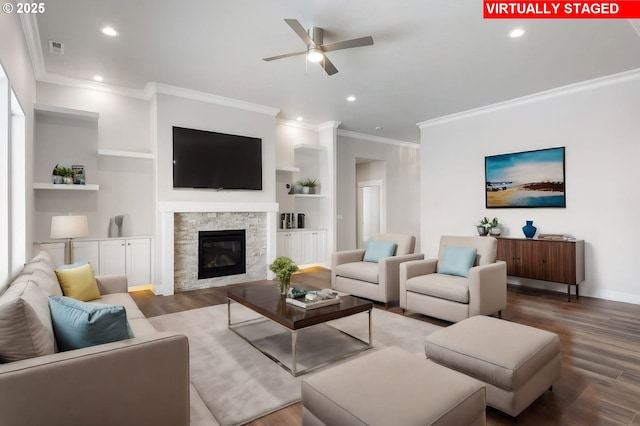 living room featuring a stone fireplace, crown molding, ceiling fan, hardwood / wood-style flooring, and built in shelves