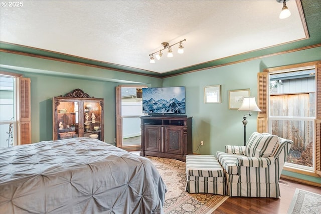 bedroom with a textured ceiling, wood finished floors, rail lighting, and crown molding