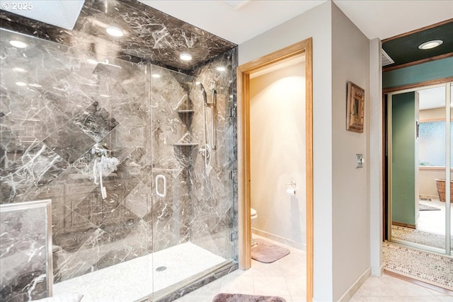 bathroom featuring toilet, a marble finish shower, baseboards, and tile patterned floors