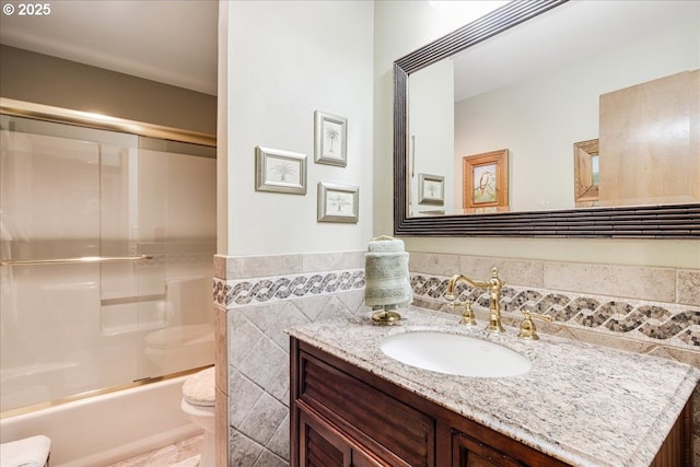 bathroom with tile walls, toilet, enclosed tub / shower combo, wainscoting, and vanity