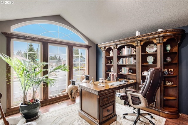 home office featuring lofted ceiling, light wood-style flooring, visible vents, and a textured ceiling