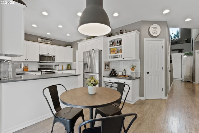 8775 SW Comanche Way, Tualatin, OR 97062 - kitchen featuring appliances with stainless steel finishes, backsplash, dark countertops, light wood-style flooring, and white cabinetry