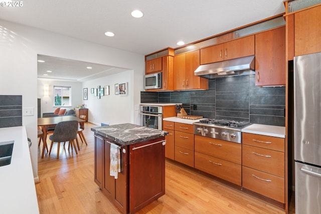 9004 SW 36th Ave, Portland, OR 97219 - kitchen with under cabinet range hood, appliances with stainless steel finishes, light wood-style flooring, brown cabinets, and recessed lighting