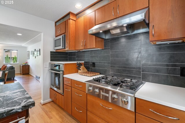 9004 SW 36th Ave, Portland, OR 97219 - kitchen with under cabinet range hood, stainless steel appliances, light wood-style flooring, brown cabinets, and recessed lighting