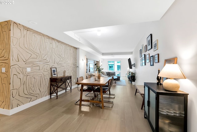 dining area with an accent wall, a tray ceiling, baseboards, and light wood finished floors