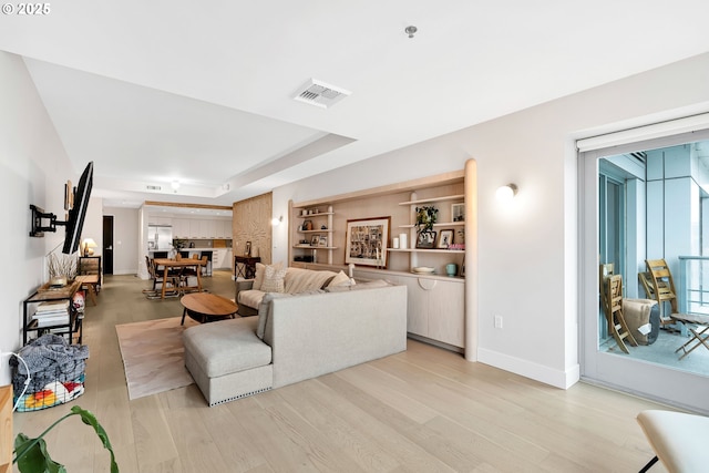 living room with baseboards, a raised ceiling, visible vents, and light wood-style floors