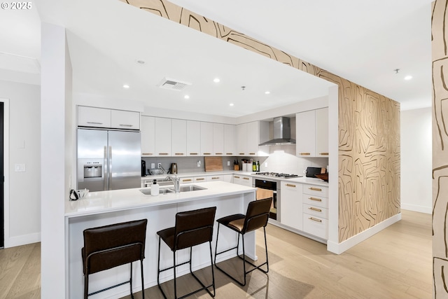 kitchen with a sink, visible vents, appliances with stainless steel finishes, wall chimney exhaust hood, and a kitchen bar