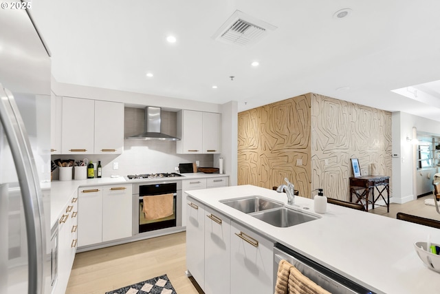 kitchen featuring visible vents, appliances with stainless steel finishes, light countertops, wall chimney range hood, and a sink