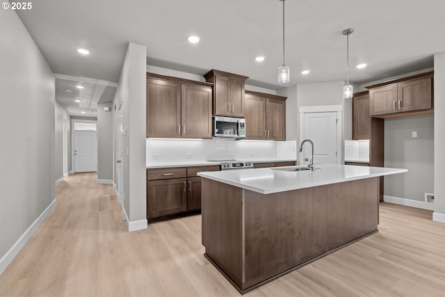 kitchen featuring pendant lighting, an island with sink, sink, backsplash, and light wood-type flooring