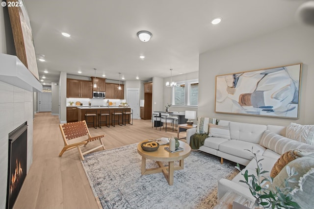 living area with recessed lighting, a warm lit fireplace, light wood-type flooring, and an inviting chandelier