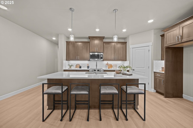 kitchen with stainless steel microwave, a center island with sink, light countertops, and a kitchen bar