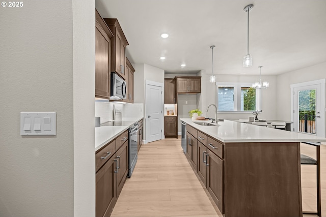 kitchen featuring light wood-type flooring, a kitchen island with sink, a sink, a kitchen breakfast bar, and appliances with stainless steel finishes