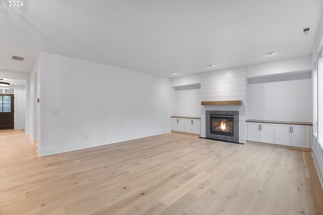 unfurnished living room with light wood-type flooring, a large fireplace, baseboards, and visible vents