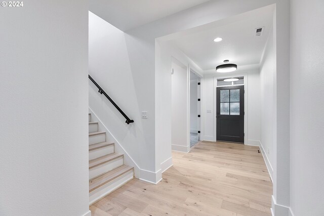 entrance foyer with light wood-style floors, baseboards, visible vents, and stairway