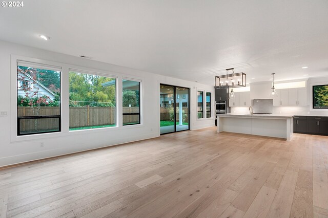 interior space featuring decorative light fixtures, light countertops, open floor plan, white cabinets, and light wood-type flooring