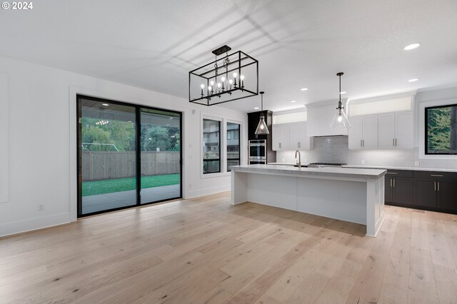 kitchen with white cabinets, light countertops, light wood-type flooring, backsplash, and an island with sink