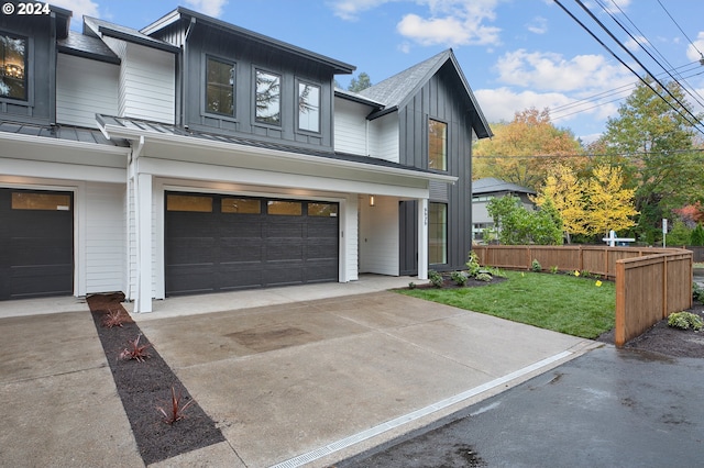 view of front facade with an attached garage, board and batten siding, a standing seam roof, fence, and driveway