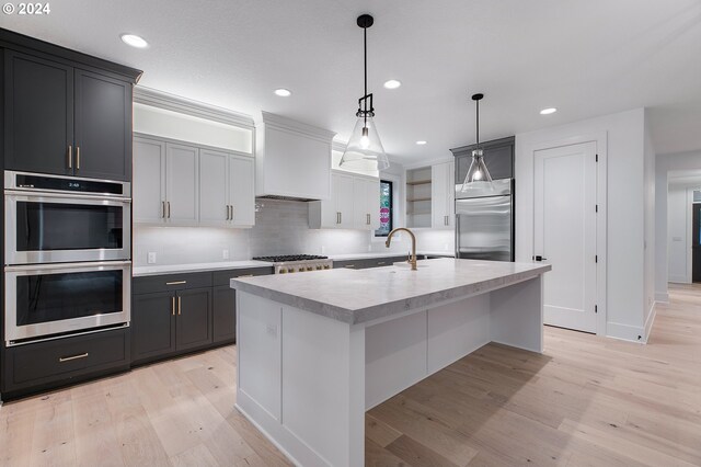 kitchen with decorative light fixtures, light countertops, custom range hood, appliances with stainless steel finishes, and light wood-type flooring