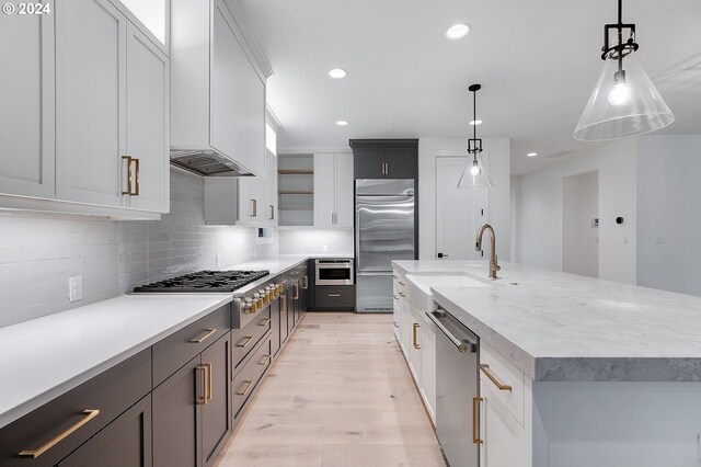 kitchen with a center island with sink, open shelves, stainless steel appliances, light wood-style flooring, and a sink