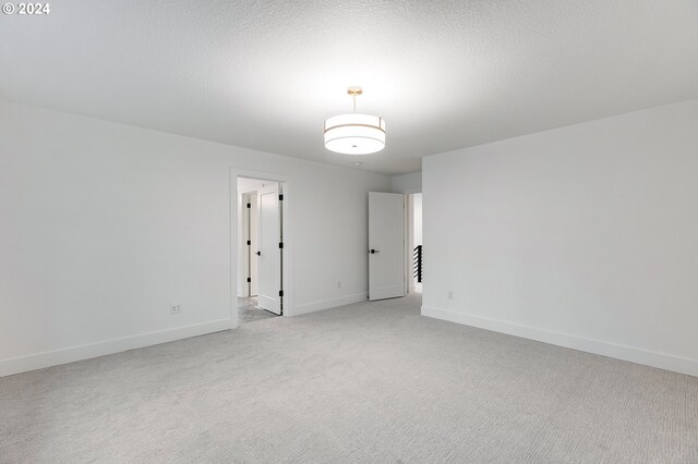 empty room with a textured ceiling, baseboards, and light colored carpet