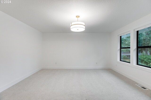 empty room featuring baseboards, visible vents, light carpet, and a textured ceiling