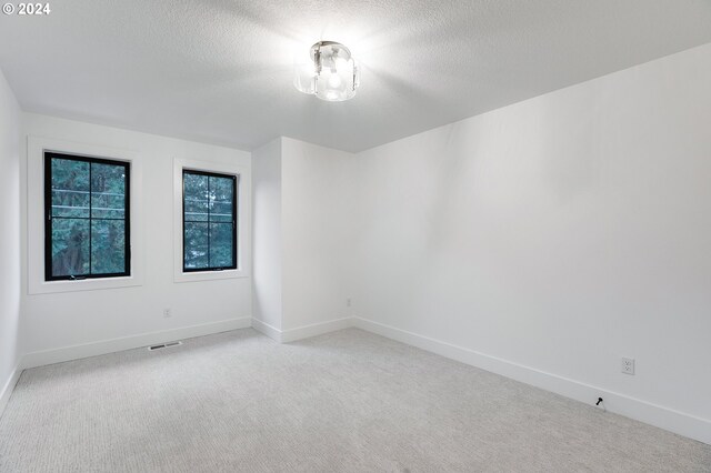 unfurnished room featuring a textured ceiling, baseboards, visible vents, and light colored carpet