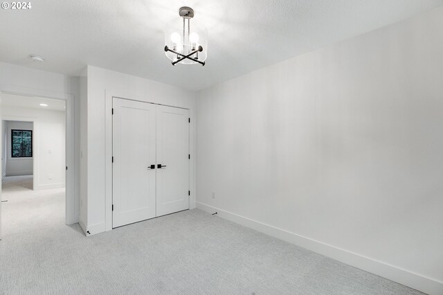 interior space featuring a closet, light carpet, a textured ceiling, a chandelier, and baseboards