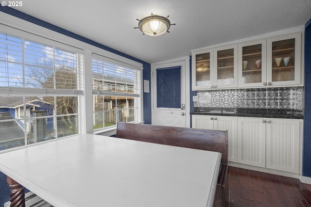 kitchen with glass insert cabinets, white cabinets, dark countertops, dark wood-type flooring, and decorative backsplash