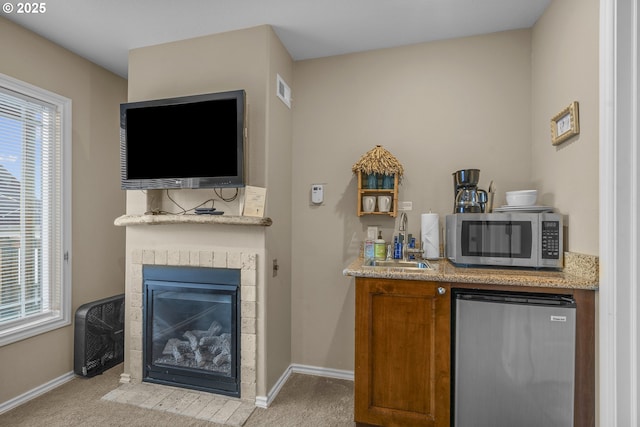 bar featuring light carpet, a sink, a glass covered fireplace, and stainless steel appliances