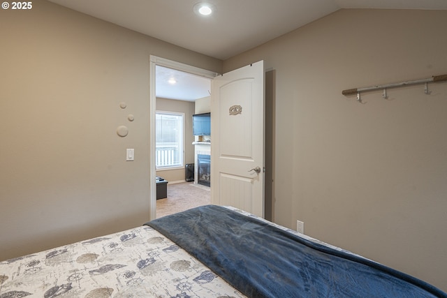 bedroom with light colored carpet, lofted ceiling, a glass covered fireplace, and recessed lighting